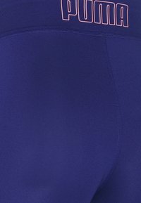 Leggings blu navy di Puma con una texture liscia. Presentano una vita alta e un logo rosa prominente sul retro. Dettagli delle cuciture presenti.