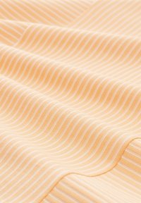 Baumwollstoff mit einer glatten Textur, der abwechselnd wellenförmige orange und weiße Streifen aufweist. Die Falten des Stoffes erzeugen sanfte Kurven und weiche Schatten.