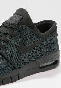 Svart mesh-sneaker med rund tå, vadderad krage och svart gummisula. Har Nike-logotyp och platta svarta skosnören.