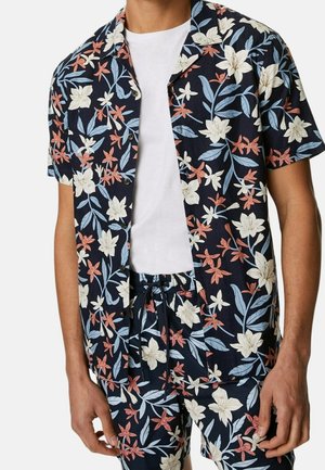 Kurzarmhemd und Shorts-Set in Marineblau mit einem floralen Muster in Weiß, Pfirsich und Blau. Der Stoff wirkt leicht und strukturiert mit einer lässigen Passform.
