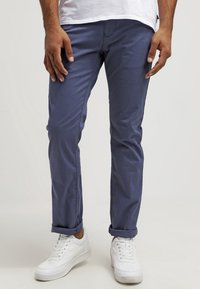 Marinblå chinos i bomullstwill, slim fit-design, framfickor, uppvikta ärmar, i kombination med vita sneakers.