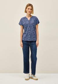 Blusa navy con motivo a foglie blu, scollatura a V e maniche corte, abbinata a jeans a gamba larga blu e sneakers bianche con dettagli blu.