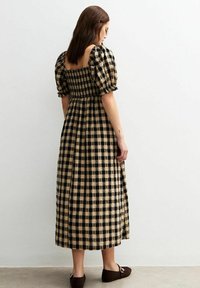Svart och beige rutmönstrad klänning med figursydd bodice, puffärmar och en kjol som går till mitten av låret. Tillverkad av texturerad tyg.
