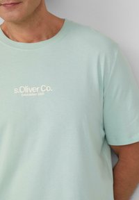 Licht mintgroen T-shirt van zacht materiaal met een ronde hals. Voorzien van een witte geborduurde logo "s.Oliver Co. Opgericht 1969" aan de voorkant.