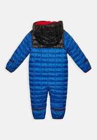 Sininen puffatakki lumipuku, jossa on musta nuppi ja punainen sisus, sisältäen vaakasuorat ompeleet, vetoketjulliset taskut ja elastiset hihnat.