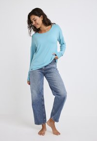 Jasnoniebieska bluzka z długim rękawem, wykonana z miękkiego materiału, w połączeniu z luźnymi, wyblakłymi niebieskimi jeansami o prostym kroju. Prosty krój bez wzorów i akcentów.