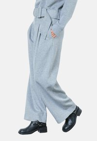 Pantalones grises de pierna ancha hechos de tela suave, con cinturón en la cintura, pliegues y bolsillos laterales, combinados con botas negras hasta el tobillo.