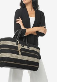 Gran bolsa de tote tejida grande con rayas negras y beige, asas de cuero negro y una cadena en tono dorado con una pieza de acento.