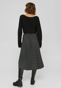 Suéter negro de mezcla de lana con un escote ancho y mangas largas, combinado con una falda larga de cuadros gris con pliegues y botas negras con cordones.