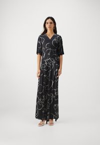 Black maxi dress with a V-neckline and short sleeves, featuring white abstract line patterns. Smooth fabric, loose fit, worn with strappy sandals.