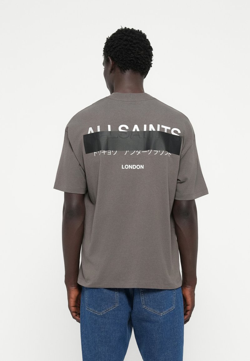 T-shirt en coton gris avec une coupe décontractée, présente un grand texte blanc "ALLSAINTS" sur le dos, ainsi qu'un panneau horizontal noir avec du texte japonais.