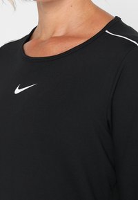 Schwarzes, sportliches Langarmoberteil aus leichtem Stoff mit einem leicht abgerundeten Ausschnitt und kontrastierenden weißen Nähten an den Schultern.