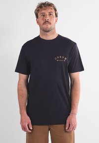 T-shirt en coton noir à manches courtes, avec un petit logo orange sur le côté gauche de la poitrine. Design classique à col rond.