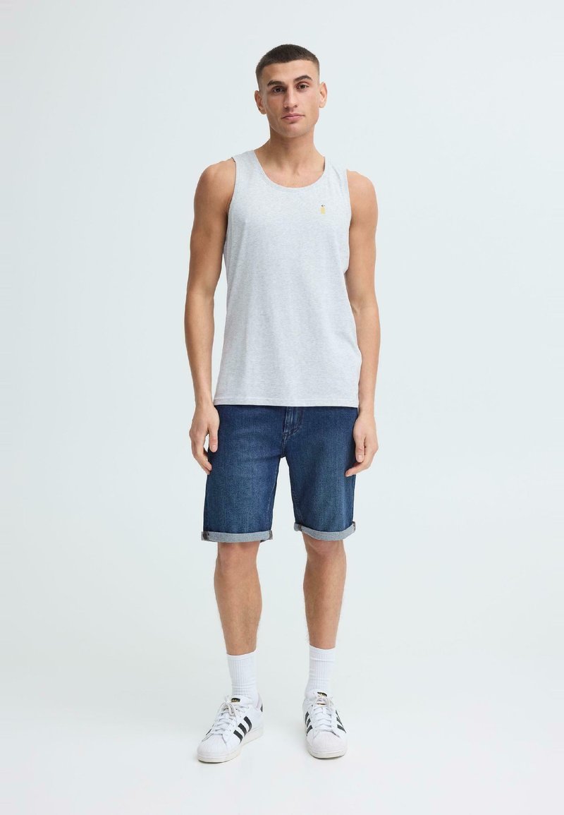 Ung mann står iført en lys grå ermeløs topp, oppbrettede denimshorts, hvite sokker og hvite joggesko med svarte striper.