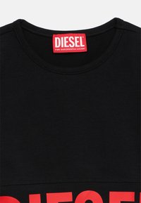 Crna majica od pamuka s crvenim logotipom i natpisom "DIESEL" sprijeda. Ima okrugli izrez i kratke rukave.