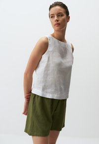 Top senza maniche bianco in lino con scollatura quadrata, abbinato a pantaloni corti verde oliva. Design semplice e tessuto leggero. Nessun motivo visibile.