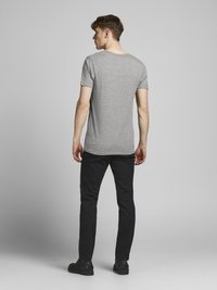 Szürke, rövid ujjú pamut póló, kerek nyakkivágással. Fekete, slim-fit nadrággal és fekete cipővel viselve, hátulról nézve.