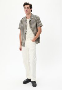 Cămașă cu mânecă scurtă, în dungi bej și albastru, asociată cu pantaloni albi și pantofi negri. Dispune de un design cu nasturi și un croi lejer.