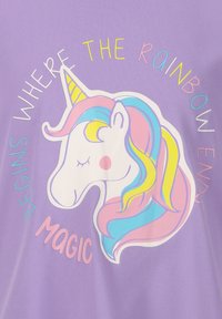 Paarse t-shirt met een eenhoornprint en een regenboogkleurige manen. De tekst luidt "Begint Waar de Regenboog Eindigt" en "Magie."