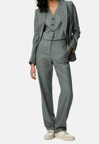 Grauer maßgeschneiderter Anzug mit einem verkürzten Blazer mit zwei Knöpfen, passender Weste, weiter Hose und weißen Sneakers.