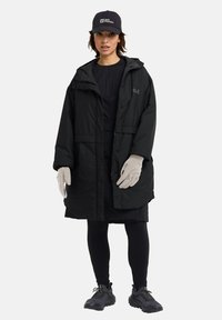 Black padded jacket with a hood, featuring a front zipper and snap closure. Worn with black leggings, gray gloves, and a branded cap.