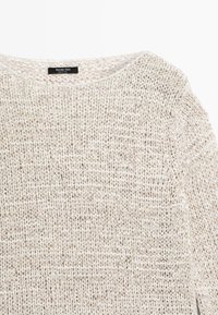 Pull en maille texturée beige et blanche avec un col rond et des manches longues, étiquette Massimo Dutti, fabriqué en Chine.