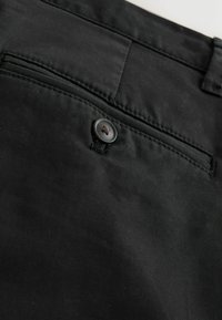 Nahaufnahme einer schwarzen Hosentasche mit sichtbarem Knopf und genähten Nähten auf Baumwollstoff.