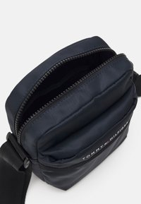 Marinblå nylonaxelväska med dragkedjeöppning, justerbar rem och broderad logotyp på framsidan. Texturerad yta, kompakta design.