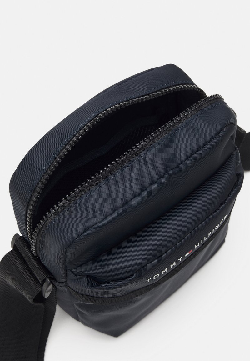 Marinblå nylonaxelväska med dragkedjeöppning, justerbar rem och broderad logotyp på framsidan. Texturerad yta, kompakta design.