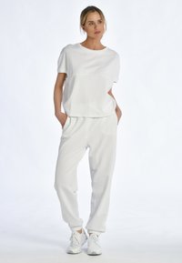 Weißes Baumwoll-T-Shirt mit kurzen Ärmeln und lockerer Passform, kombiniert mit weißen Jogginghosen. Beide Kleidungsstücke haben eine glatte Textur und ein minimalistisches Design.