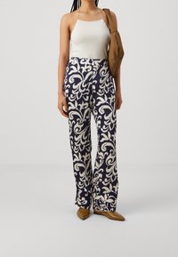 Marinblå och gräddformade mönstrade vida byxor med blommönster, kombinerade med en vit linne och en brun axelväska. Bruna spetsiga ballerinaskor.