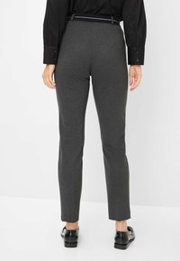 Pantaloni grigio scuro su misura con una vestibilità slim, caratterizzati da una superficie liscia e una vita nera, abbinati a scarpe nere lucide.