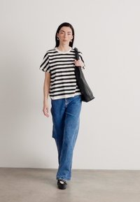 Tricou cu dungi alb-negru, cu mâneci scurte, asortat cu blugi albastri largi din denim. Modelul poartă o geantă tote neagră și pantofi negri.