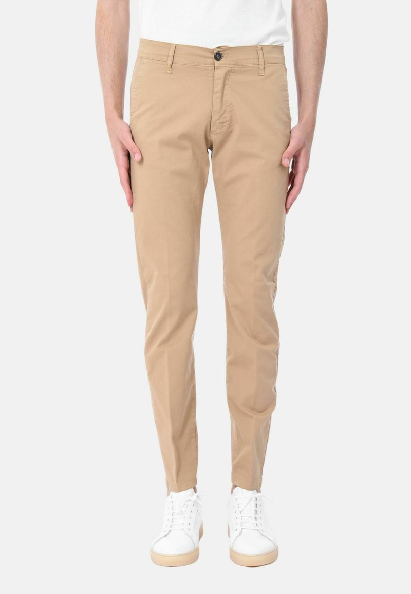 Chinos khaki in cotone, con vestibilità slim, chiusura con bottone e tasche laterali, abbinati a sneakers bianche.