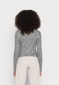 Camisola de malha cinza de mangas longas com um padrão texturizado, design ajustado e punhos canelados. Combinada com calças largas de cores claras.
