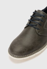 Gray leather shoe with a textured surface, round toe, navy laces, and white rubber sole. Features a perforated pattern along the upper.
