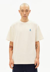 Crèmewit T-shirt met korte mouwen gemaakt van katoen, met een lichtblauw lintlogo op de borst. Gladde textuur, losse pasvorm.