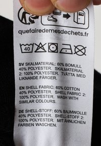 Etichetta di cura con istruzioni per la cura e composizione del tessuto: 60% cotone, 40% poliestere; sfondo nero; testo in più lingue.