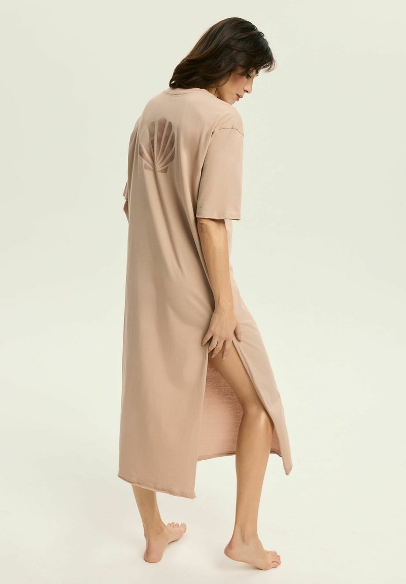 Długa beżowa sukienka wykonana z miękkiego materiału, z bocznym rozcięciem i wzorem liści na plecach. Luźny krój z krótkimi rękawami.