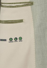 Beige stof met olijfgroene accenten, voorzien van een gestructureerd patroon. Inclusief labels voor gerecycled materiaal, duurzaamheid en milieuvriendelijkheid.