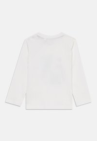 T-shirt en coton blanc à manches longues avec col rond, design uni, et trois boutons au niveau du col dans le dos. Texture lisse.