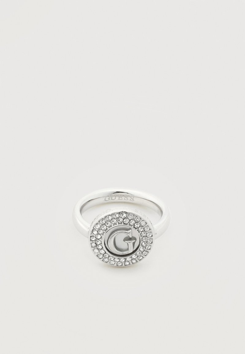 Bague en argent avec un visage rond présentant un "G" en relief au centre, entouré de deux rangées de petits cristaux clairs.