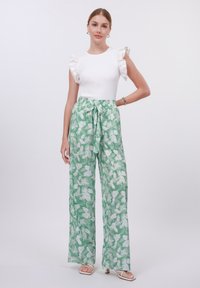 Top blanco de canalé con mangas con volantes; pantalones verdes de pierna ancha con patrones de hojas blancas y detalle de cinturón anudado. Sandalias completaron el look.