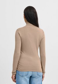 Maglione beige a collo alto con maniche lunghe, design aderente, trama a coste e finitura liscia, abbinato a jeans in denim blu.