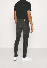 Slimmade svarta jeans med fem fickor, subtila blekningar och en läderlapp på midjan. Bärs med vita sneakers.