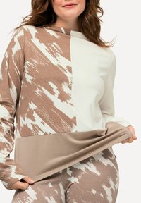 Langärmliges Oberteil mit einem zwei Farbdesign in Beige und Weiß, das ein strukturiertes Muster und einen weichen, fließenden Stoff aufweist.