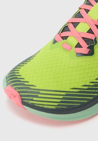 Neon green athletic shoe with pink laces and black accents. Features textured upper and geometric pattern along the sole.