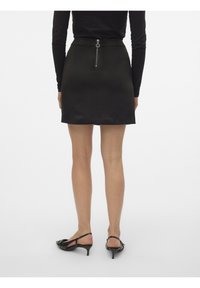 Mini-jupe en satin noir au design élégant, fermeture éclair au dos et silhouette ajustée, associée à des sandales noires à talons.