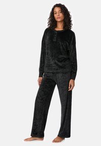 Conjunto de ropa de descanso negro que incluye una camiseta de manga larga con abertura de botones y pantalones anchos a juego, ambos con un acabado texturizado y estampado.