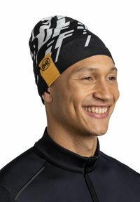 Black beanie with white abstract patterns and a yellow Buff logo patch. Made from soft material, designed for comfort and warmth.